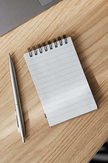 Top view of a spiral notebook and pen on a wooden desk, perfect for stationery themes. HD phone wallpaper