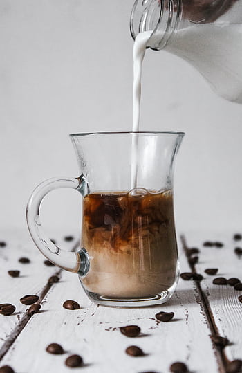 Glass mug of coffee with milk being poured, surrounded by scattered coffee beans on a wooden table. HD phone wallpaper