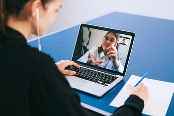 Woman participating in a virtual meeting, taking notes during a video conference on a laptop. HD wallpaper