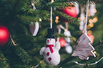 Close-up of a festive snowman ornament hanging on a Christmas tree branch with lights. HD wallpaper