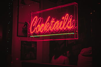Bright neon 'Cocktails' sign glowing in a lively Dublin bar at night. HD wallpaper