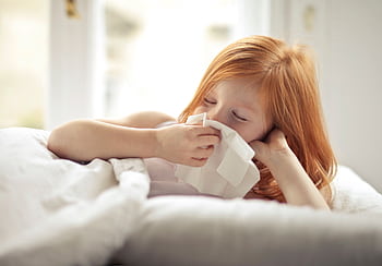 Redheaded child resting in bed, wiping nose with tissue, unwell with flu-like symptoms. HD wallpaper