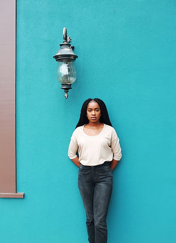 A fashionable woman poses confidently against a vibrant turquoise wall outdoors. HD phone wallpaper