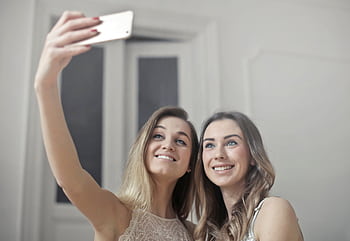 Two smiling women capturing a joyful selfie indoors, showcasing friendship and happiness. HD wallpaper