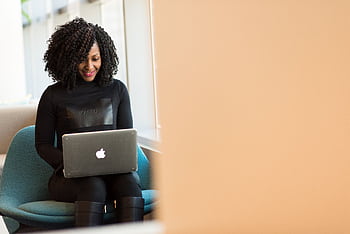 African American woman happily working on a laptop in a modern office setting. HD wallpaper