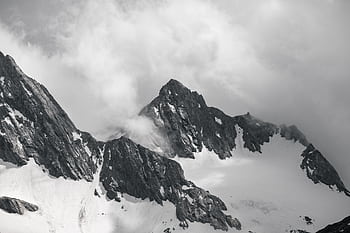 Dramatic black and white capture of Tirol's rugged mountain peaks enveloped in mist and clouds. HD wallpaper