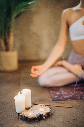 Woman practicing meditation in lotus pose with candles and incense, focusing on wellness and relaxation. HD phone wallpaper