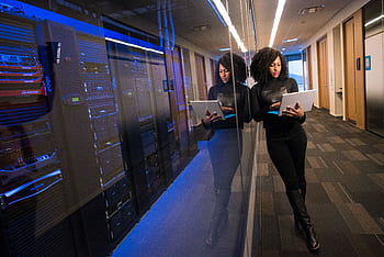 A woman using a laptop navigating a contemporary data center with mirrored servers. HD wallpaper