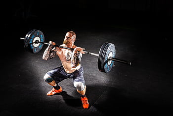 A muscular man performing a power clean exercise in a dimly lit gym. HD wallpaper