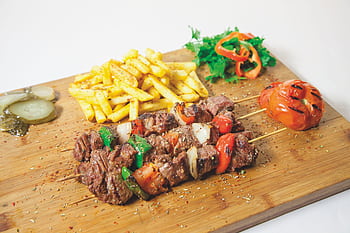 Delicious grilled shashlik served with seasoned french fries and fresh vegetables on a wooden board. HD wallpaper
