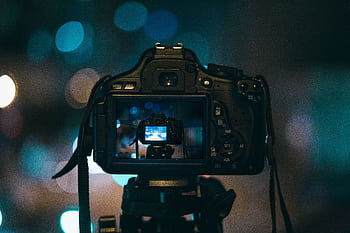 Close-up of a DSLR camera capturing a bokeh background in a dimly lit setting, illustrating night graphy. HD wallpaper