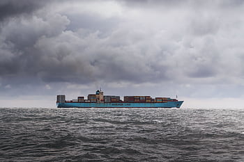 A large cargo ship carrying containers on a cloudy ocean horizon. HD wallpaper
