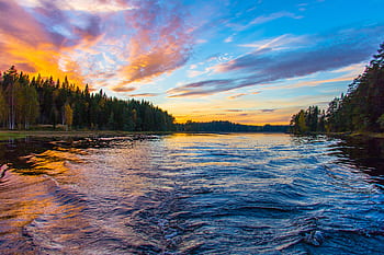 Peaceful lake scene capturing a vibrant sunset sky with lush forest surrounds and tranquil water ripples. HD wallpaper