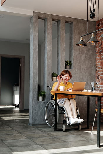 Woman in a wheelchair enjoying remote work and video call at home in a modern interior. HD phone wallpaper