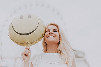 Cheerful woman holding a smiley balloon outdoors on a sunny day, exuding happiness and positivity. HD wallpaper