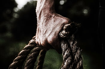 A close-up shows a strong, firm hand gripping a thick, rough rope, showcasing strength and determination in an outdoor setting. HD wallpaper