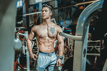Shirtless man with tattoos posing in a gym environment, showcasing fitness and strength. HD wallpaper