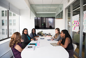 Five diverse women collaborating in a modern office meeting room, discussing projects. HD wallpaper