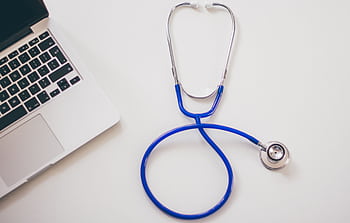 Medical stethoscope and laptop on a white desk, symbolizing digital health solutions. HD wallpaper
