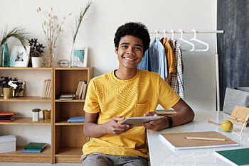 Smiling teenager using a tablet at his desk for online learning at home. HD wallpaper