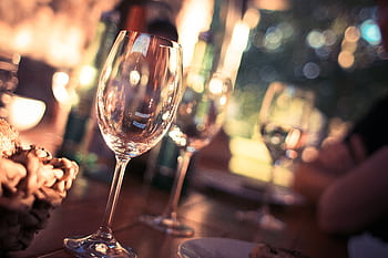 Close-up of wine glasses on a dining table with bokeh lights, creating a warm and inviting atmosphere. HD wallpaper