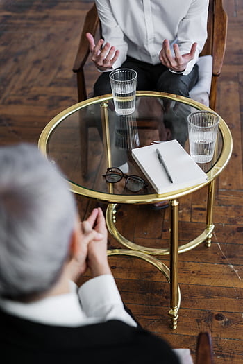 Two adults discussing mental health in a counseling session across a glass table indoors. HD phone wallpaper