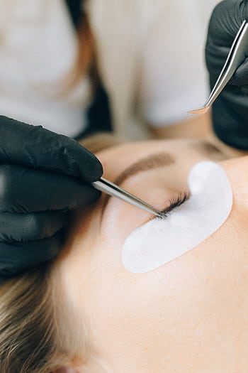 Black-gloved technician applying eyelash extensions to a woman's eye in a beauty salon setting. HD phone wallpaper