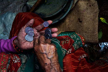 Close-up of an elderly woman's hands counting coins on a colorful textile background. HD wallpaper