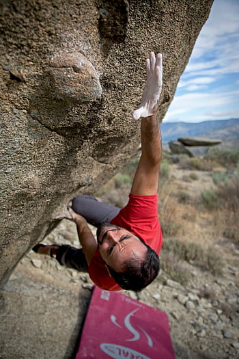 Man in red shirt bouldering on a steep rock face, showcasing strength and determination. HD phone wallpaper
