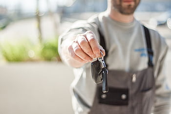 Hand holding a car key outdoors, blurred background, shallow focus. HD wallpaper