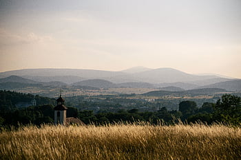 Tranquil landscape of Kamienna Góra, Poland, featuring lush fields, hills, and a distant church under a sunset sky. HD wallpaper