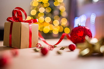 A beautifully wrapped Christmas gift with festive decorations and bokeh lights in the background, creating a warm holiday atmosphere. HD wallpaper