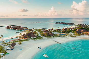 Stunning aerial view of a luxurious tropical resort in the Maldives, showcasing overwater bungalows and turquoise waters. HD wallpaper