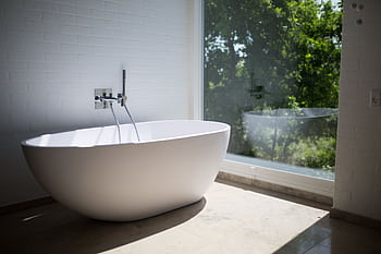 Sleek white bathtub by large window in sunlit minimalist bathroom setting. HD wallpaper