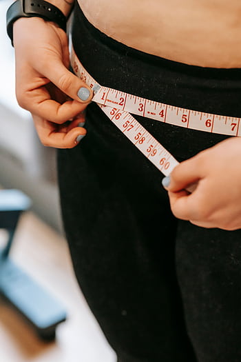 Woman measuring waist with tape for fitness and weight loss goals. HD phone wallpaper