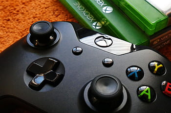 Xbox controller close-up with game cases on orange background. HD wallpaper