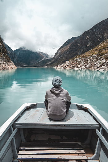 Contemplative view of a person on a boat in a serene lake surrounded by mountains in Huaraz, Peru. HD phone wallpaper