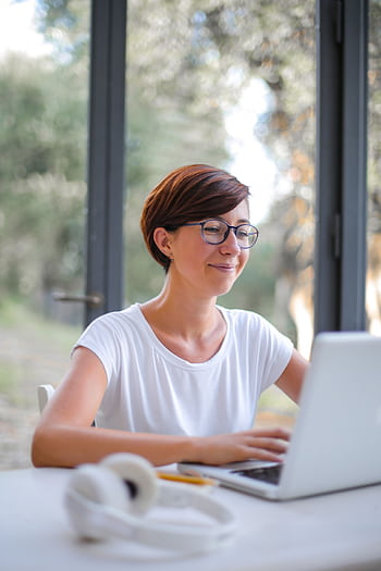 A happy woman with short hair using a laptop indoors, showcasing remote work lifestyle. HD phone wallpaper