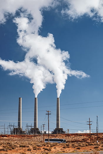 Tall smokestacks at an industrial plant with smoke against a blue sky. HD phone wallpaper