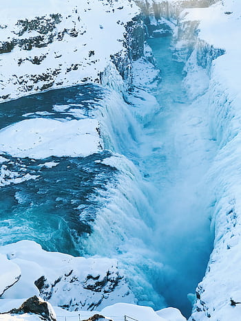 Stunning view of a frozen waterfall cascading through a snowy Icelandic gorge, capturing winter's icy beauty. HD phone wallpaper