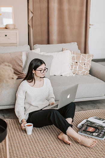 A young woman sits comfortably on the floor with a laptop and a cup of tea, enjoying a leisurely moment indoors. HD phone wallpaper