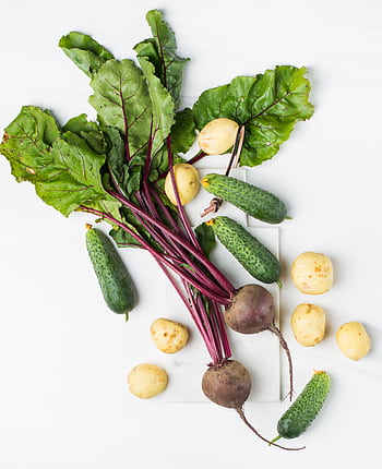 Assorted organic vegetables including beets, cucumbers, and potatoes on a white surface. HD phone wallpaper
