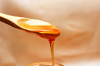 Macro shot of golden honey pouring from a wooden spoon, emphasizing its rich texture and color. HD wallpaper