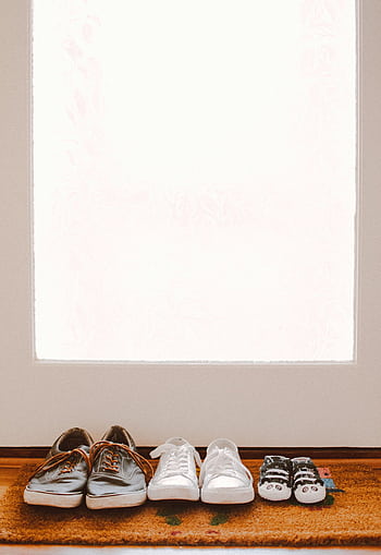 A collection of family shoes, including baby booties, on a welcoming mat by the door. HD phone wallpaper