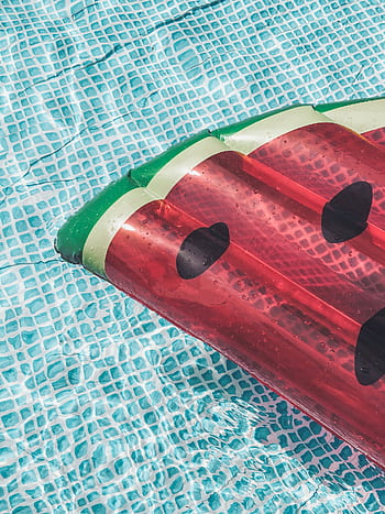 A vibrant watermelon-shaped inflatable float on clear blue water in a swimming pool, perfect for summer leisure. HD phone wallpaper