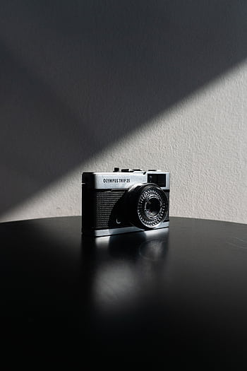 Close-up of a vintage Olympus Trip 35 camera in dramatic lighting on a black table. HD phone wallpaper