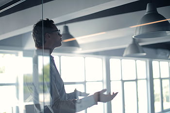 Business professional giving a presentation in a modern office setting through glass. HD wallpaper