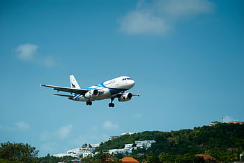 A passenger airplane descends for landing over lush hills in sunny Thailand. HD wallpaper