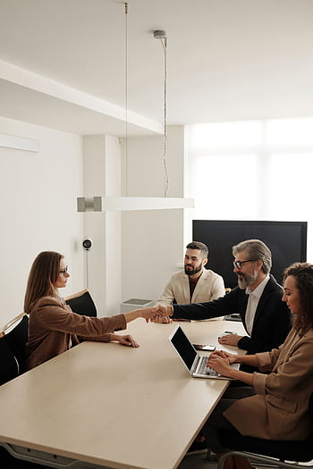 Business professionals engaging in a handshake across a conference table, signifying successful collaboration. HD phone wallpaper