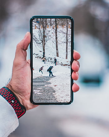 Hand holding smart displaying a winter scene with people walking on snow-covered path. HD phone wallpaper